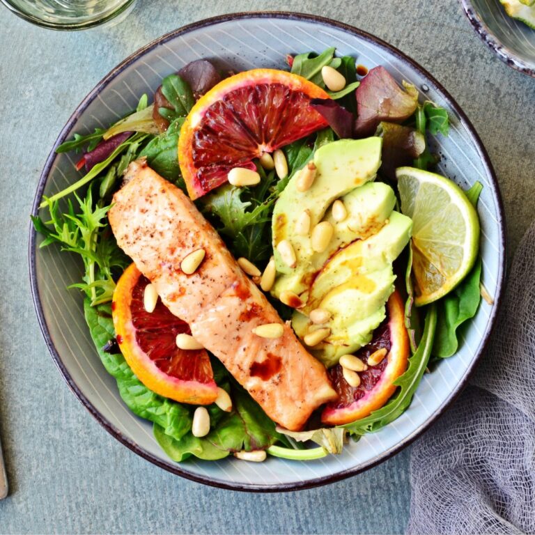 A healthy ketogenic meal with avocado, grilled salmon, leafy greens, and nuts, representing the variety of foods in the keto diet.