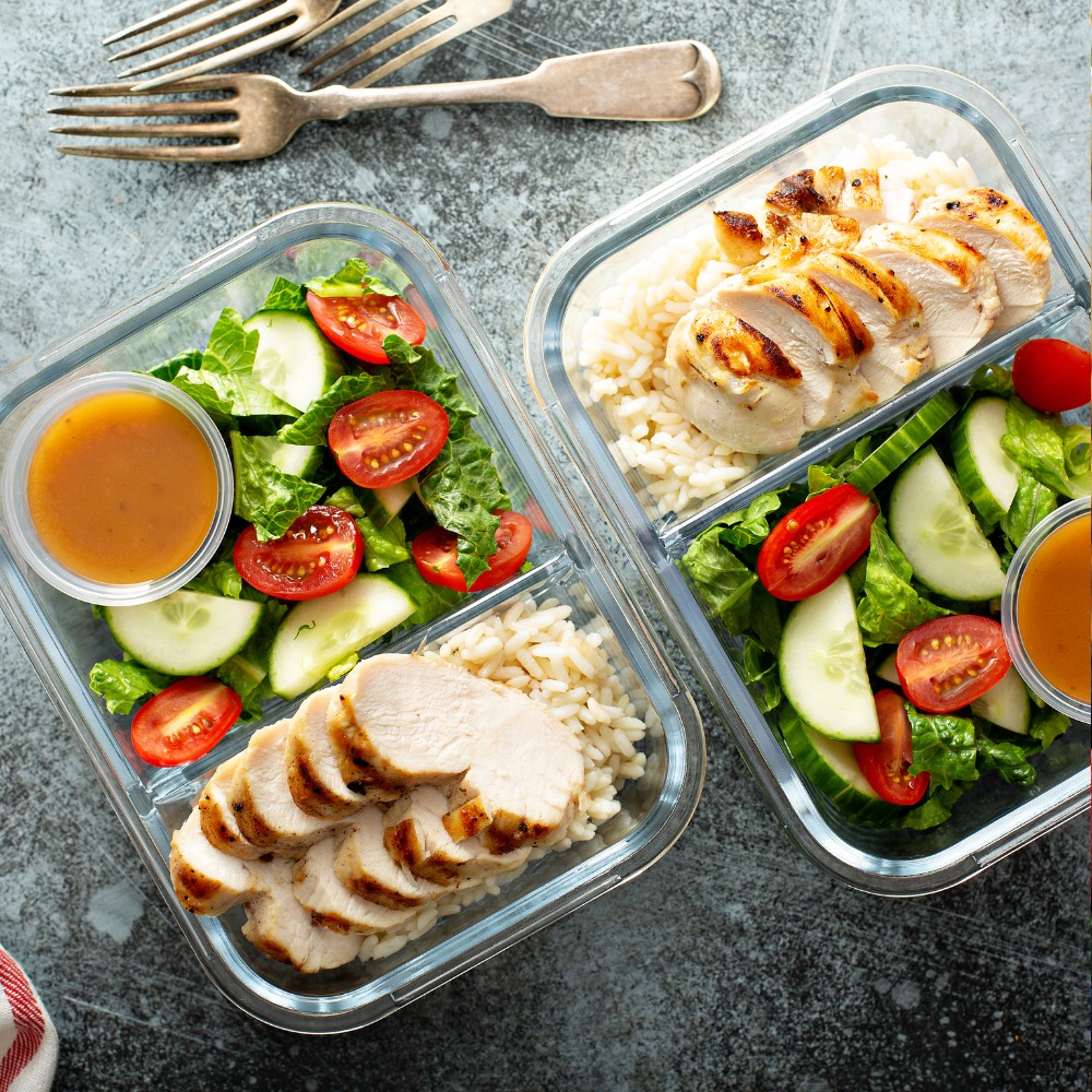 An organized layout of prepped Mediterranean meals in containers, including salads, grilled chicken, and vegetable dishes.