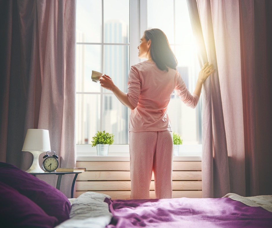 A photo of a person standing by a large window, bathed in morning sunlight, or an outdoor scene during sunrise. 