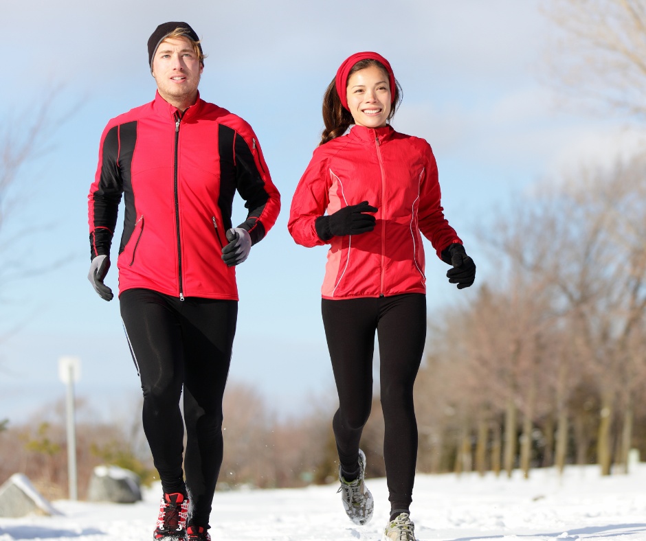 Two friends jogging in winter workout gear, staying motivated by exercising together outdoors in a snowy setting.