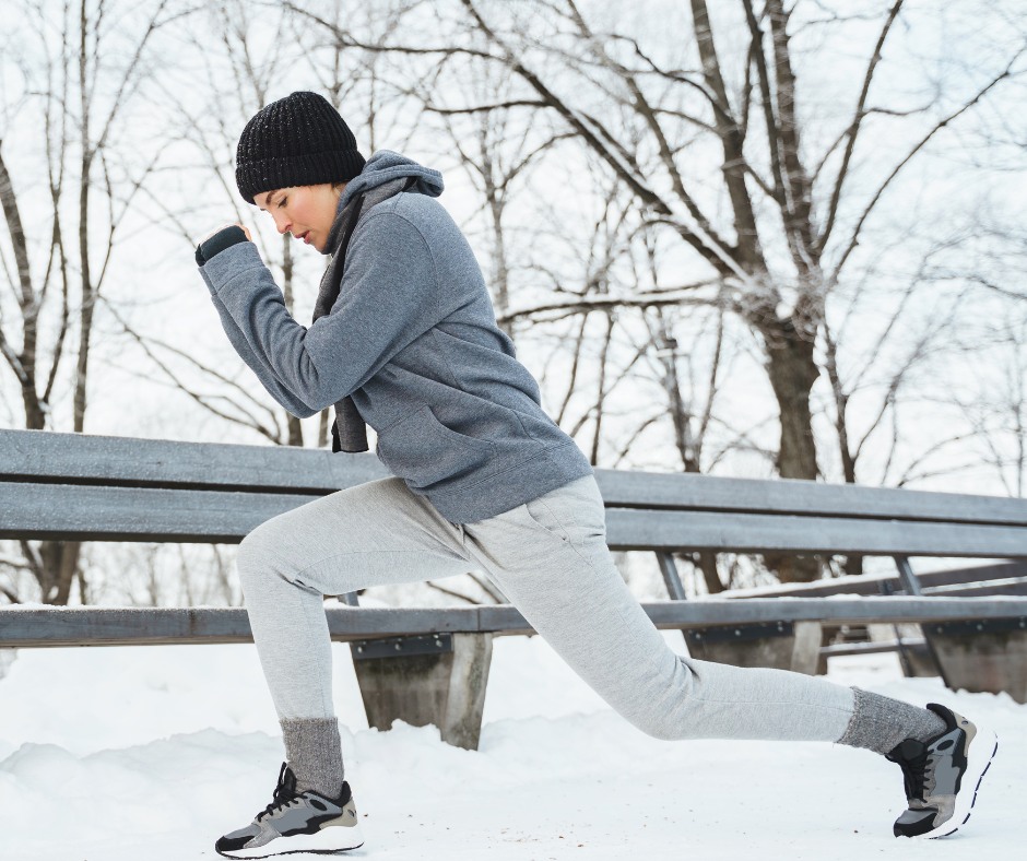 Person jogging on a snowy path during winter sunrise, dressed in warm workout clothes.