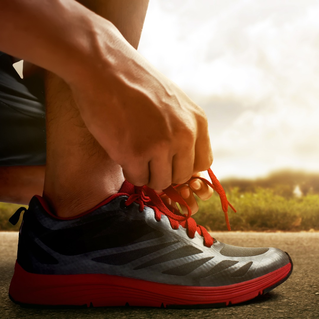 Person tying running shoes with sunrise, symbolizing consistency in workout routine.