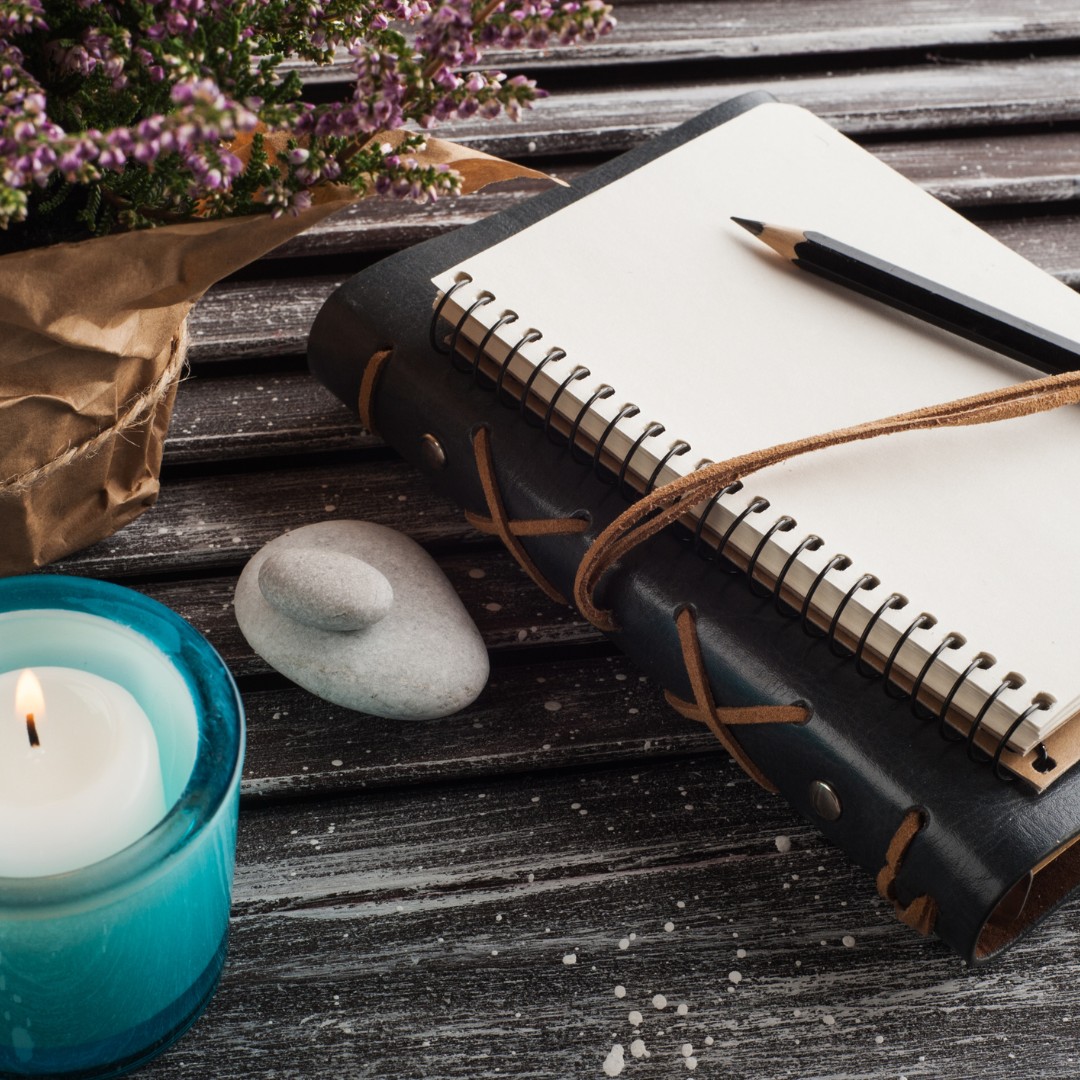 A cozy journal, pen, and candle on a wooden table, symbolizing reflective self-care practices.