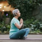 Senior woman practicing yoga outdoors in a serene garden setting, embodying peace and mindfulness.