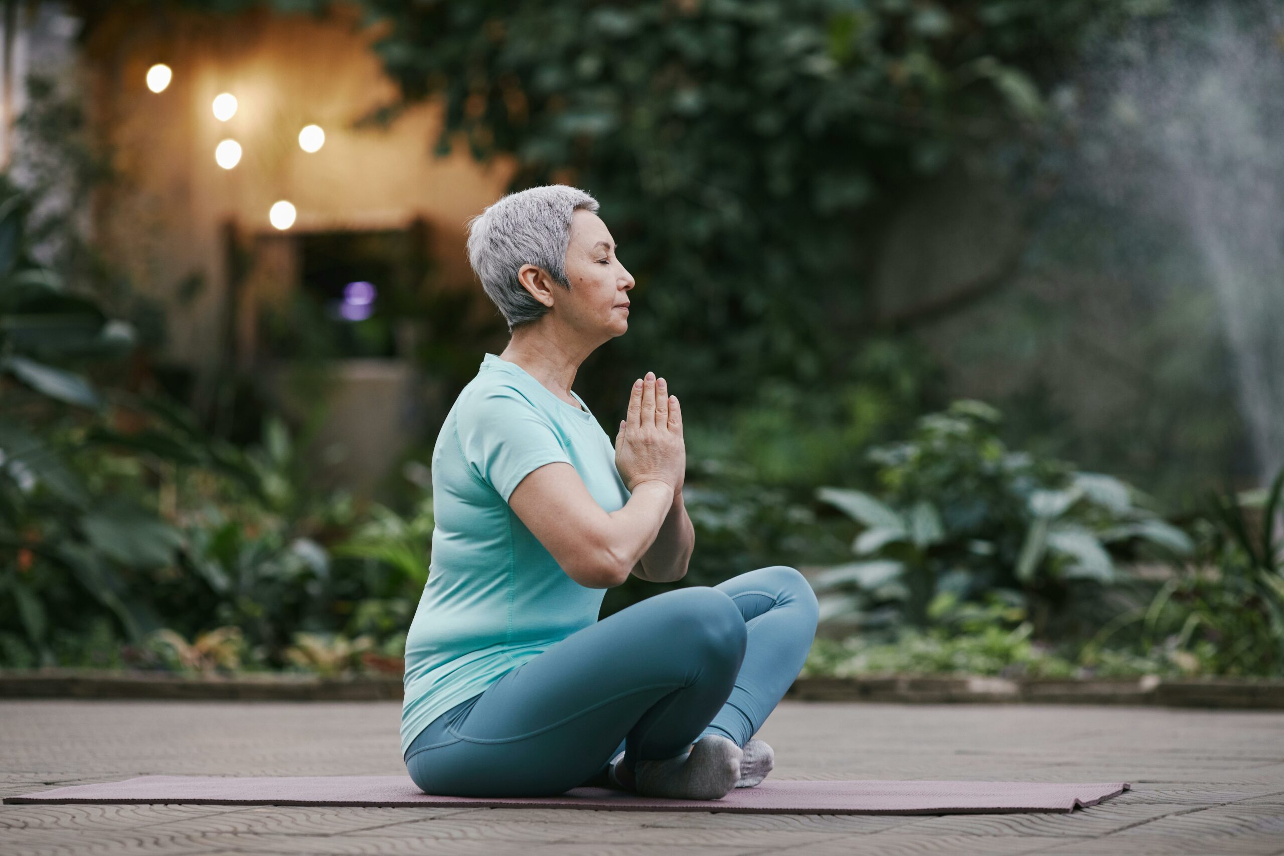 Senior woman practicing yoga outdoors in a serene garden setting, embodying peace and mindfulness.