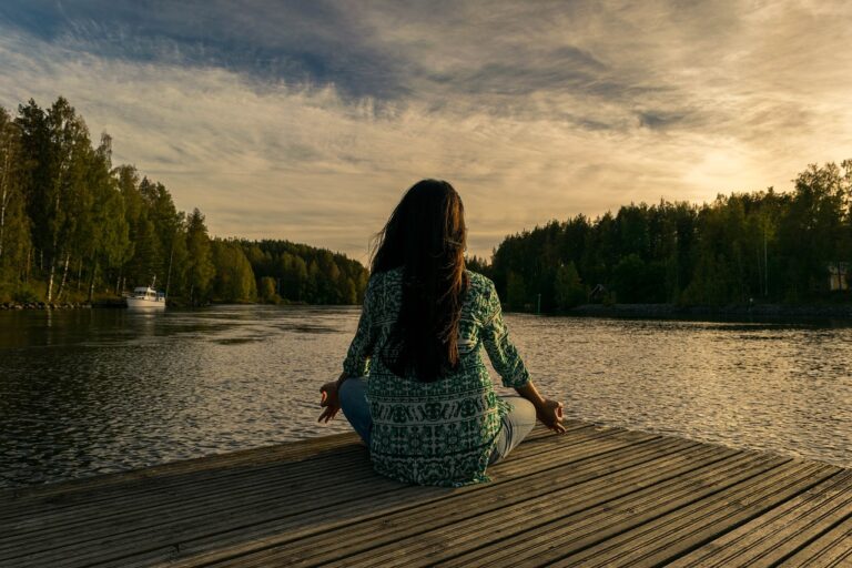 A serene scene of a person sitting cross-legged outdoors on a grassy field