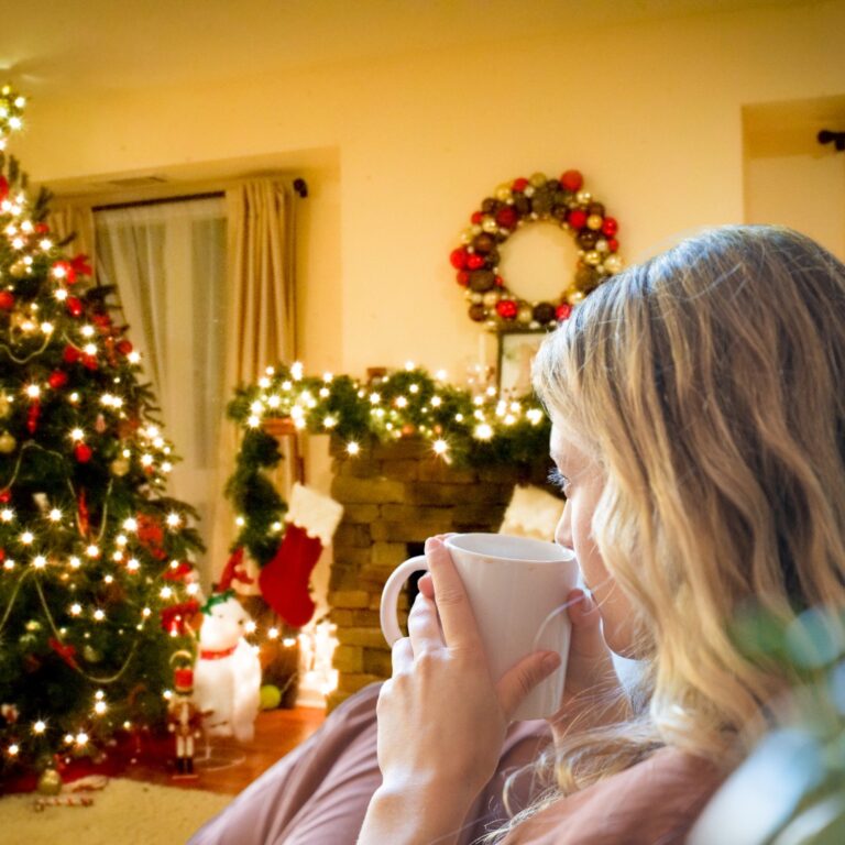 A person calmly enjoying a quiet moment at a table with holiday decorations and a warm drink."