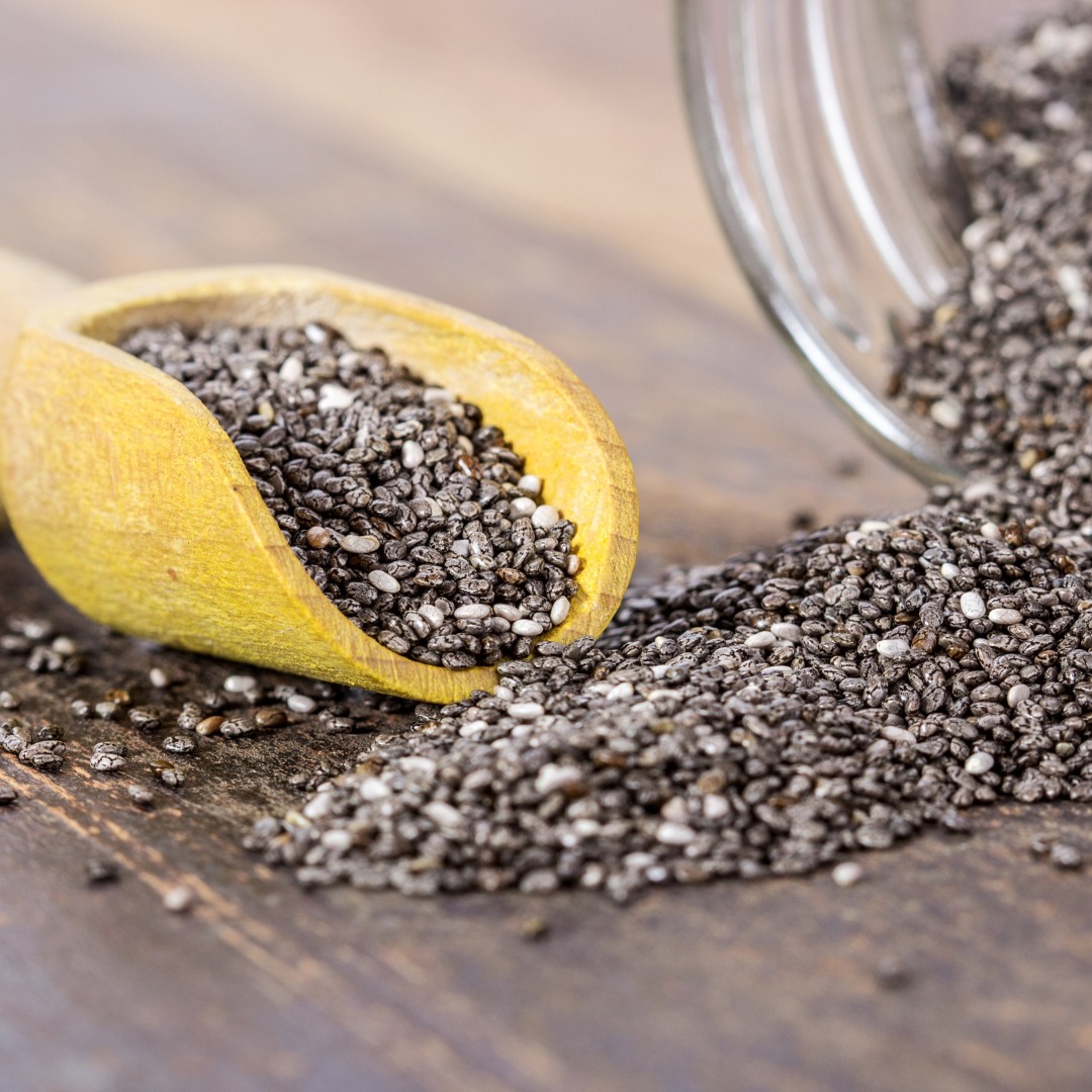 Chia seeds scattered on a marble countertop next to a jar of almond milk and fresh berries.