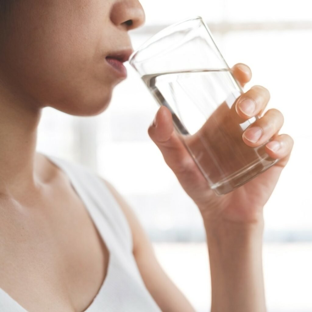 Person drinking water with fruits for hydration tips.