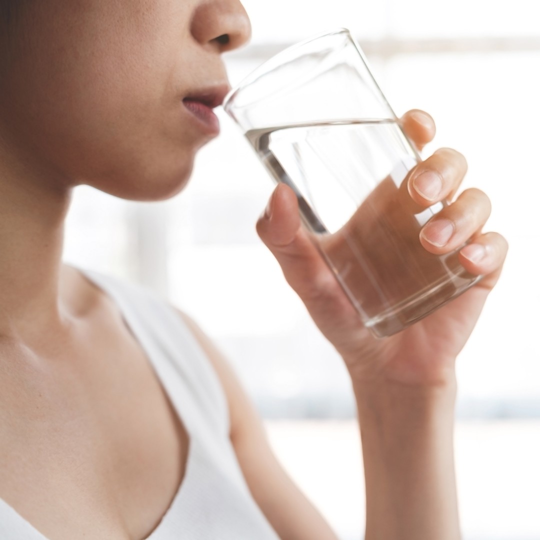 Person drinking water with fruits for hydration tips.