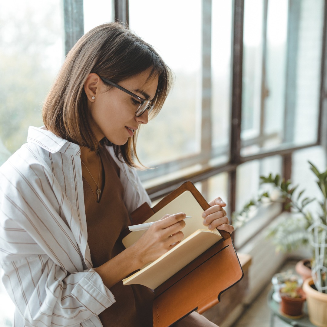 A person writing in a journal with a serene expression, representing the practice of gratitude journaling. Individual writing in a gratitude journal with a peaceful demeanor.