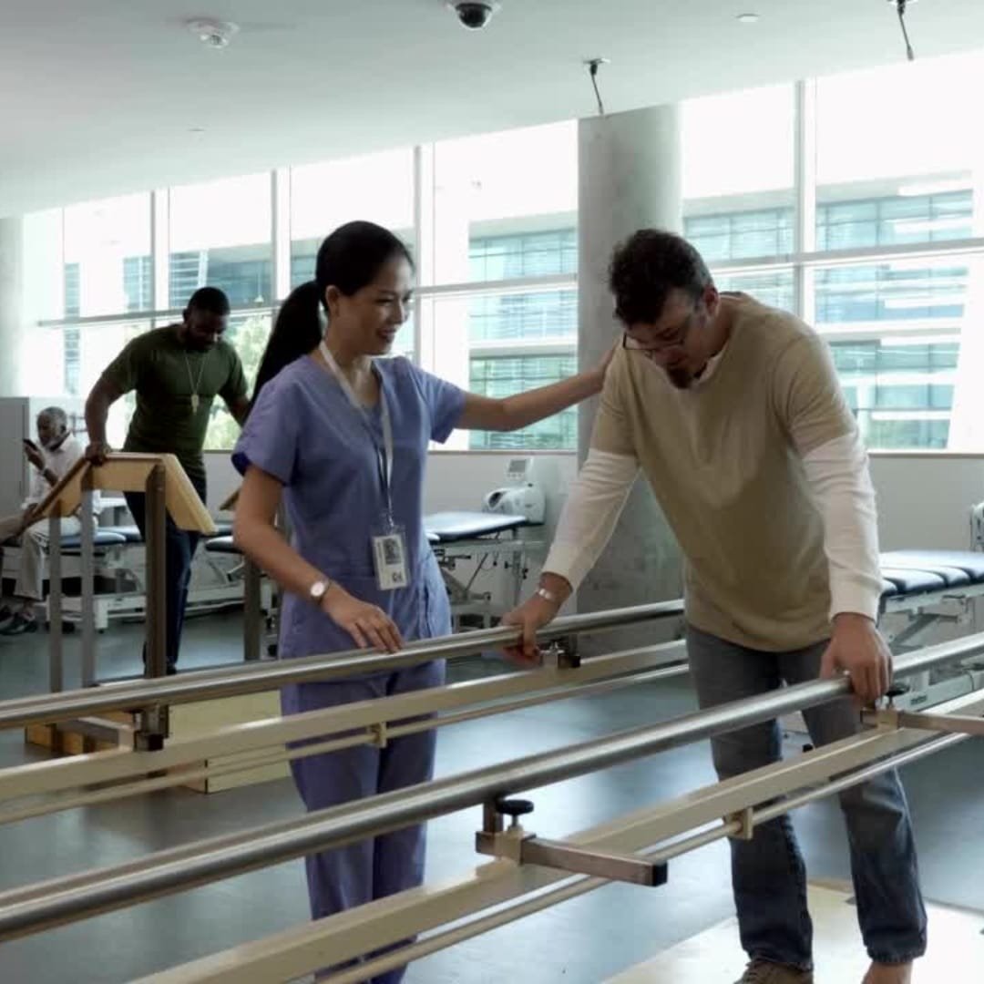 Physical therapist supporting a patient walking Patient in rehab taking first steps with a walker, supported by a therapist.